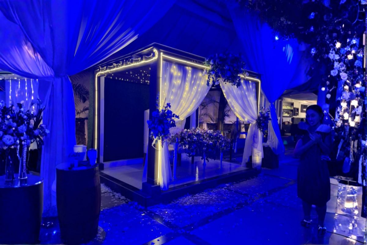 Cabana de novios con cortinas blancas, luces cálidas y arreglos florales en ambiente azul para boda nocturna en Jardín Allegra 55, Cuernavaca