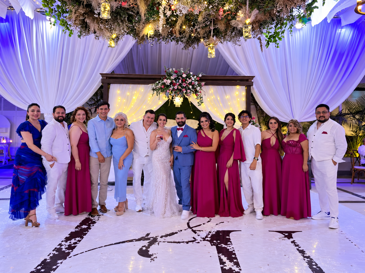 Novios brindando con familiares y cortejo en la pista de baile con iluminación violeta en Jardín Allegra 55