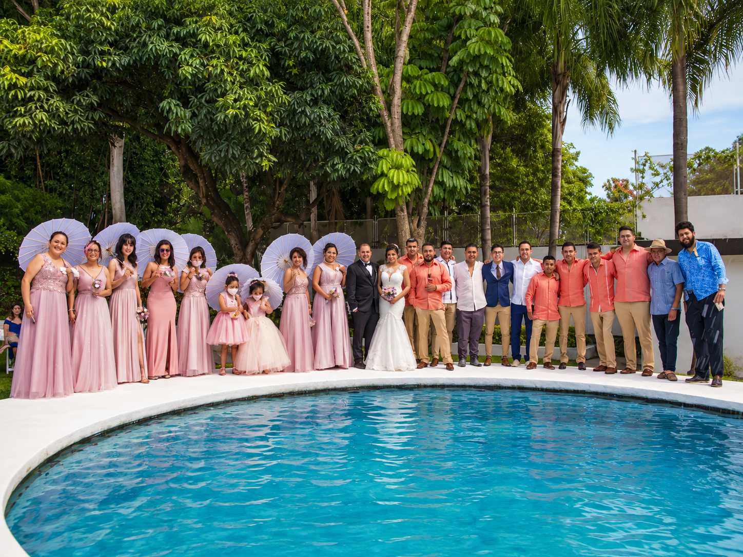 Familia y cortejo con parasoles posando junto a la alberca en una boda en Jardín Allegra 55, Cuernavaca