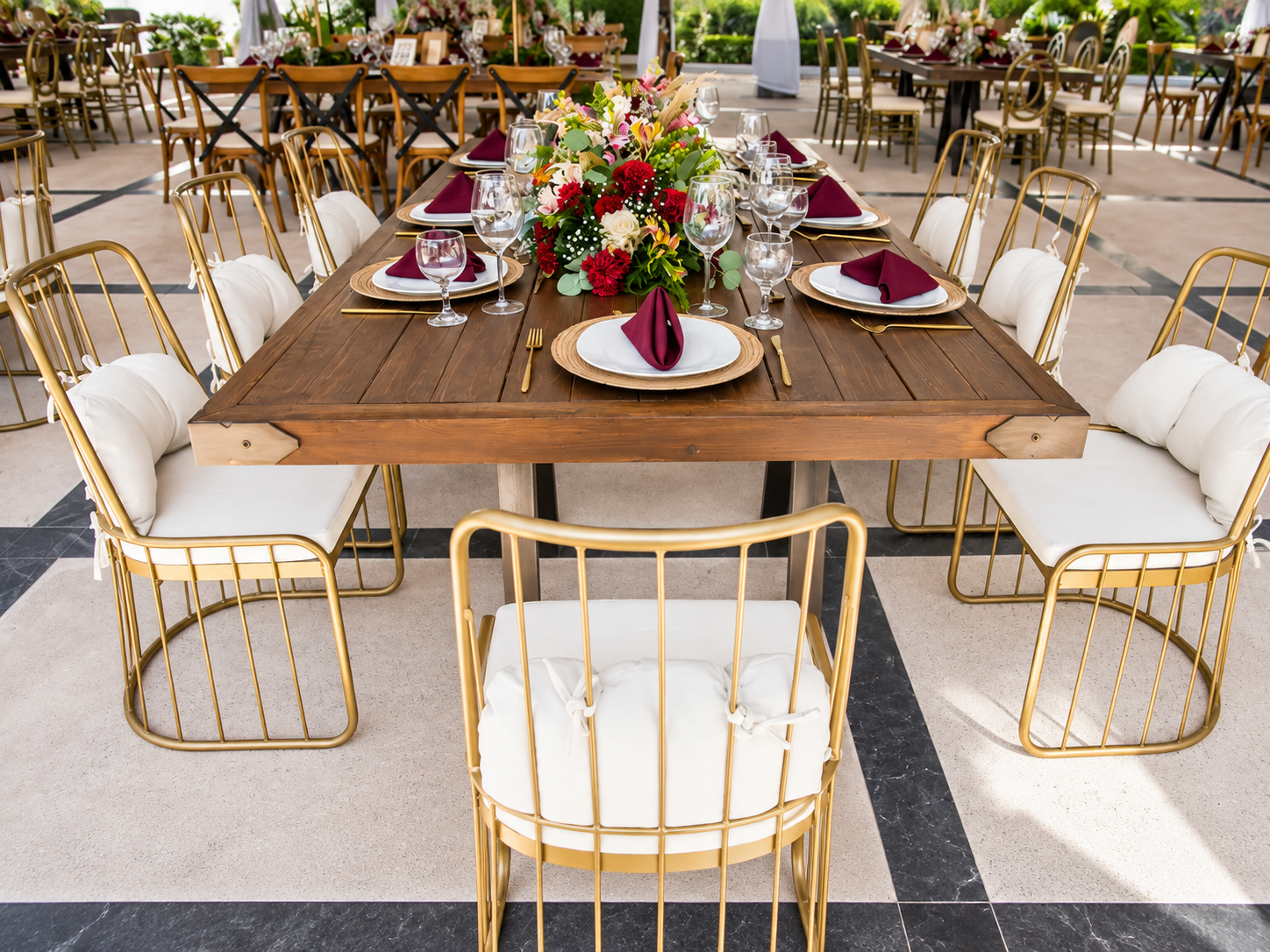 Mesas de boda con sillas doradas, servilletas vino y centros florales rojos en Jardín Allegra 55