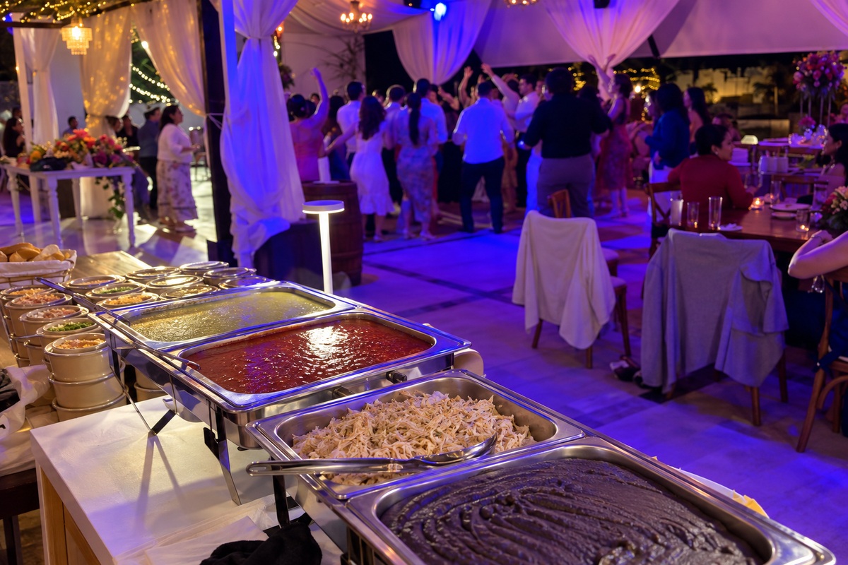 Barra de chilaquiles en primer plano e invitados bailando al fondo bajo la carpa iluminada de Jardín Allegra 55.