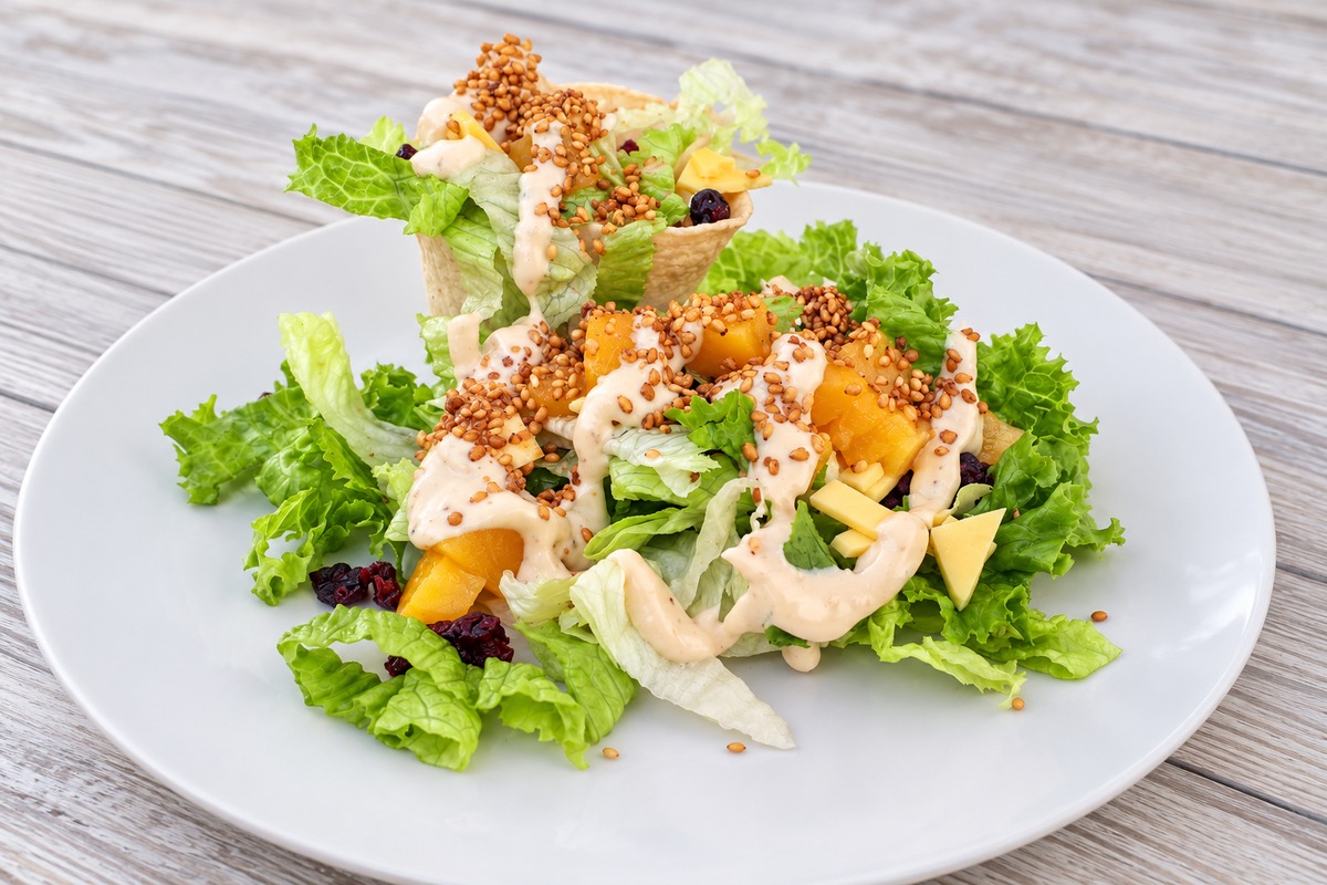 Ensalada de lechugas con fruta, queso, frutos secos y aderezo cremoso, servida con una canastita crujiente.
